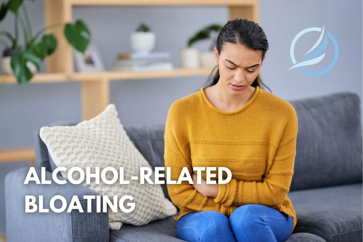 an image of a female sitting on a couch holding her stomach from alcohol related bloating.